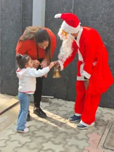 Happy child ringing a bell with Santa Claus at Shemford Gurugram during Christmas celebration.